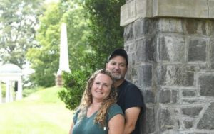 Brandon Wolslegel standing with his wife Jen in front of a concrete pillar.